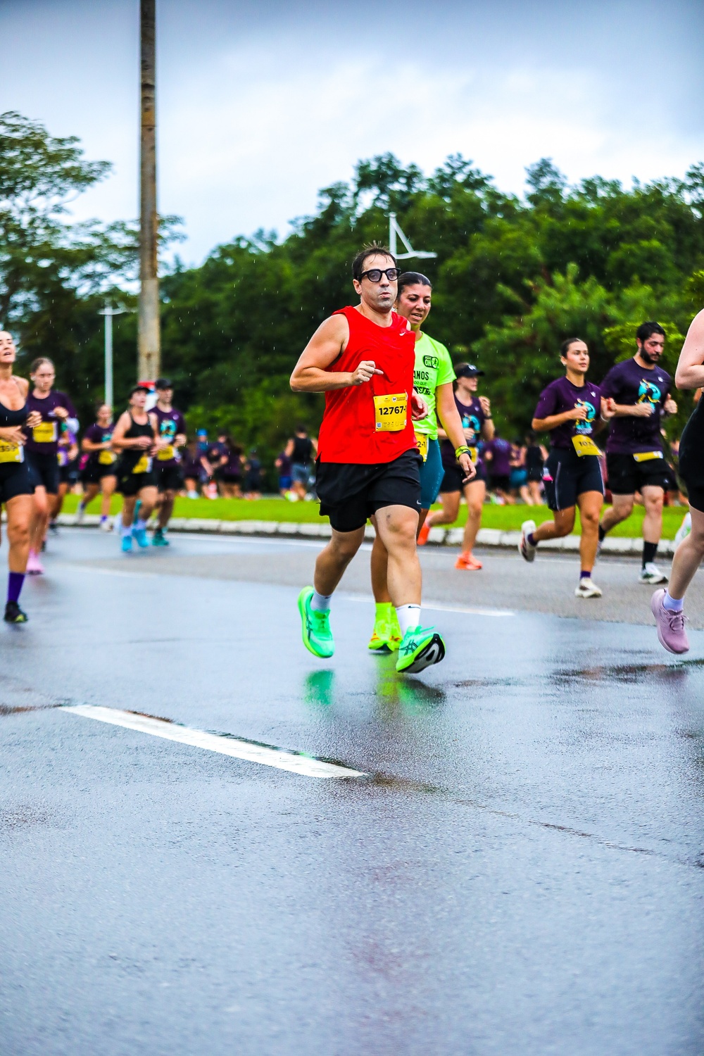Atleta correndo de regata vermelha Nike e Asics Megablast verde fluorescente em pista molhada de chuva durante os 10k da Meia Oakberry